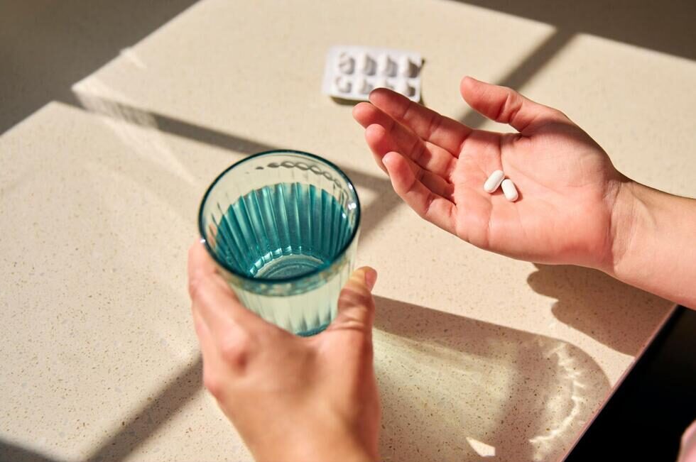 錠剤が2錠とコップに入った水を手に持っている様子