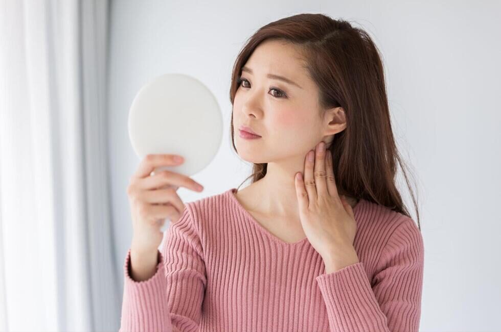 鏡で顎関節症による見た目の変化を確認する女性