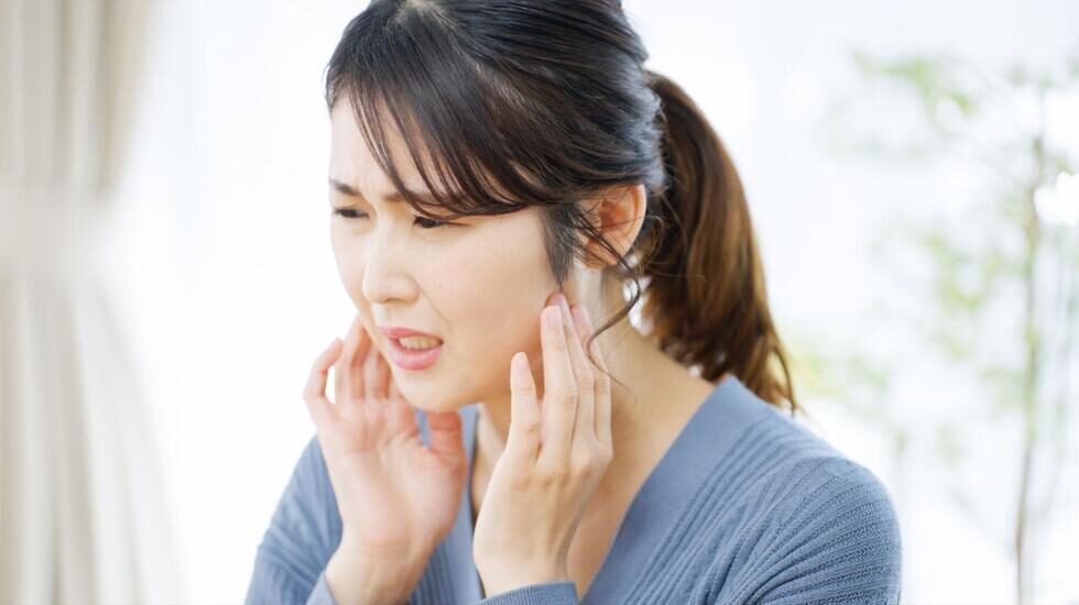 顎の付け根を両手を押さえて痛そうにする女性