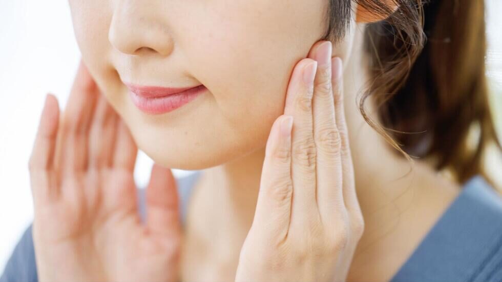 両顎の付け根を両手で押さえている口元